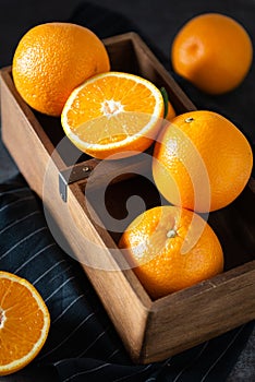 Fresh juicy oranges in a basket or box. Oranges on dark stone background. Pile of oranges, side view, close up. Healthy clean