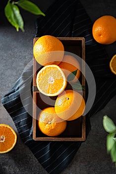 Fresh juicy oranges in a basket or wooden box. Oranges on dark stone background. Pile of oranges top view, flat lay. Healthy clean