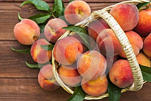 Fresh juicy peaches with leaves in a wicker basket on a wooden background. Freshlypicked peaches in a wicker basket