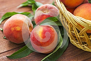 Fresh juicy peaches with leaves in a wicker basket on a wooden background. Freshlypicked peaches in a wicker basket