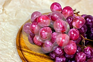 Fresh juicy pink and purple grape berries ripe in a bunch on wooden background.