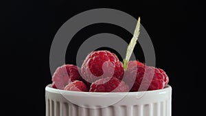 Fresh juicy raspberries in a cup - rotate on black background