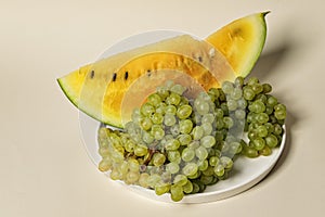 Fresh juicy slice of yellow watermelon and sweet quiche-mish grapes on a beige background. Organic vegetables and fruits