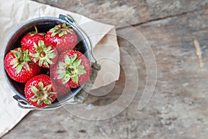 Fresh juicy strawberry in a bucket on a wooden background, top v