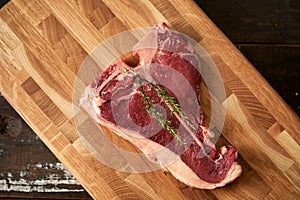 A fresh, juicy t-bone steak with a sprig of rosemary on top of a butt chopping board. Top view, place for text. Cooking prime meat