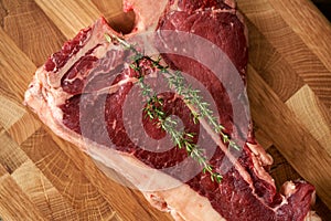 A fresh, juicy t-bone steak with a sprig of rosemary on top of a butt chopping board. Top view, place for text. Cooking prime meat