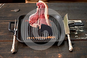 Fresh, juicy t-bone steak in a standing position with a black blank card in a grill pan with sprinkled paprika and dried tomatoes