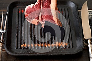 Fresh, juicy t-bone steak in a standing position with a black blank card in a grill pan with sprinkled paprika and dried tomatoes