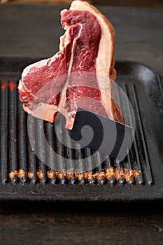 Fresh, juicy t-bone steak in a standing position with a black blank card in a grill pan with sprinkled paprika and dried tomatoes