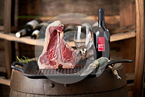 Fresh, juicy t-bone steak in a standing position on a grill pan with a bottle of red wine and a glass