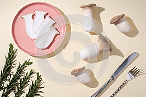 Fresh king oyster mushrooms, slices on a pink plate, rosemary sprigs, knife, fork on a yellow background in sunlight