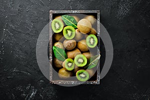 Fresh kiwi and green leaves in a wooden box on the old background. Fruits. Top view.