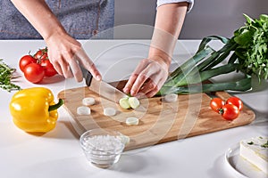 Fresh leek slices cut into the hands of a female cook on a wooden board on the kitchen table around a variety of organic