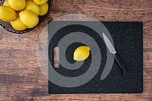 Fresh lemon on a black cutting board, wood table, basket of lemons, paring knife
