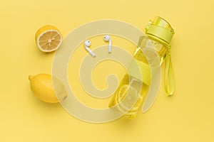 Fresh lemon, water bottle and wireless headphones on a yellow background