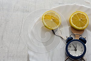 Fresh lemon on white plate, cutlery and alarm clock served for dinner or lunch
