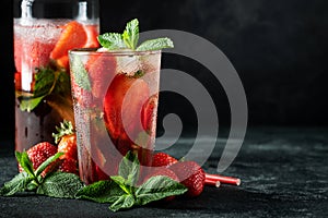 Fresh lemonade with ice, mint and strawberry on top in glass on black table background, copy space. Cold summer drink