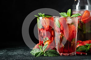 Fresh lemonade with ice, mint and strawberry on top in glass on black table background, copy space. Cold summer drink. Sparkling