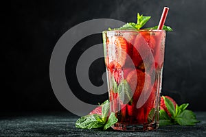 Fresh lemonade with ice, mint and strawberry on top in glass on black table background, copy space. Cold summer drink. Sparkling