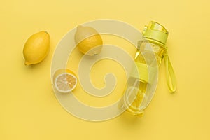 Fresh lemons and a bottle of water with lemon on a yellow background