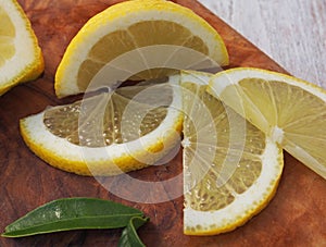 Fresh lemons on a cutting board placed on a wooden table. In the foreground one lemon cut in half.