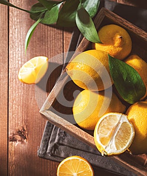 Fresh lemons with leaves in a wooden box on a dark board background close up. Citrus fruits for freshly squeezed lemonade. Dark
