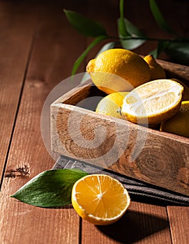 Fresh lemons with leaves in a wooden box on a dark board background close up. Citrus fruits for freshly squeezed lemonade. Dark