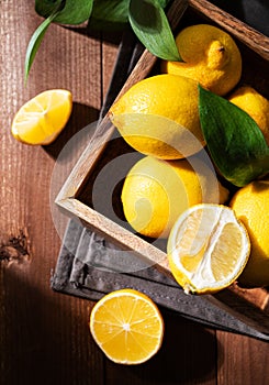 Fresh lemons with leaves in a wooden box on a dark board background close up. Citrus fruits for freshly squeezed lemonade. Dark