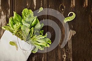 Fresh Lettuce leaveson in a paper bag a wooden dark table. Batavia salad