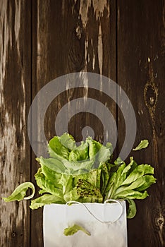 Fresh Lettuce leaveson in a paper bag a wooden dark table. Batavia salad