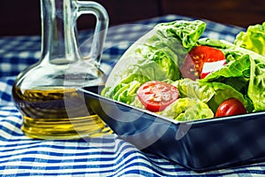 Fresh lettuce salad with cherry tomatoes radish and carafe with olive oil on wooden table.