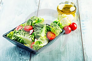 Fresh lettuce salad with cherry tomatoes radish and carafe with olive oil on wooden table.