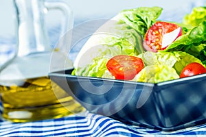 Fresh lettuce salad with cherry tomatoes radish and carafe with olive oil on wooden table.