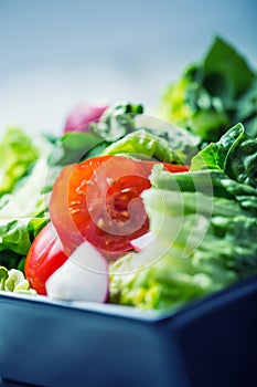 Fresh lettuce salad with cherry tomatoes radish and carafe with olive oil on wooden table.