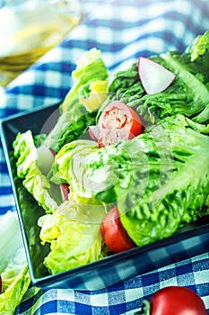 Fresh lettuce salad with cherry tomatoes radish and carafe with olive oil on wooden table.