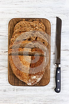 A fresh loaf of bread and a bread knife on a rustic old white table. slice of bread