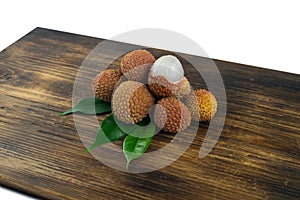 Fresh lychee and peeled showing the red skin and white flesh with green leaf on a wooden background. Lychi with leaves - tropical photo