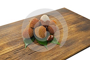 Fresh lychee and peeled showing the red skin and white flesh with green leaf on a wooden background. Lychi with leaves - tropical photo