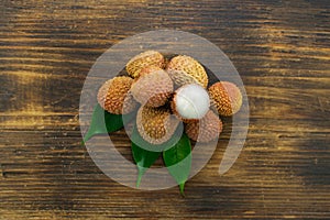 Fresh lychee and peeled showing the red skin and white flesh with green leaf on a wooden background. Lychi with leaves - tropical photo