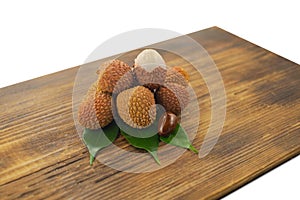 Fresh lychee and peeled showing the red skin and white flesh with green leaf on a wooden background. Lychi with leaves - tropical photo