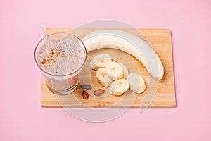 Fresh made banana smoothie in a glass on pink background