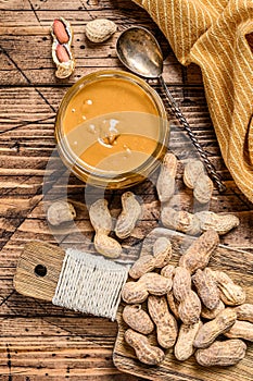 Fresh made creamy Peanut Butter in a glass jar. Wooden background. Top view