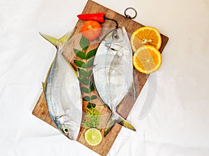 Fresh Malabar Trevally fish decorated with herbs and fruits on a wooden pad ,Isolated on white Background.Selective focus