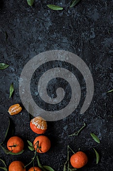 Fresh mandarin oranges with leaves on textured dark background with copy space. Top view.