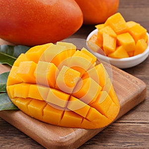 Fresh mango, beautiful chopped fruit with green leaves on dark wooden table background. Tropical fruit design concept. Flat lay.