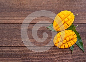 Fresh mango - beautiful chopped fruit with green leaves on dark wooden timber background. Tropical fruit design concept. Flat lay