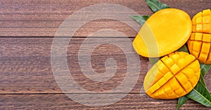 Fresh mango - beautiful chopped fruit with green leaves on dark wooden timber background. Tropical fruit design concept. Flat lay