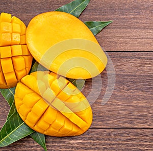 Fresh mango - beautiful chopped fruit with green leaves on dark wooden timber background. Tropical fruit design concept. Flat lay