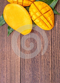 Fresh mango - beautiful chopped fruit with green leaves on dark wooden timber background. Tropical fruit design concept. Flat lay