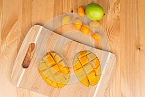 Fresh mango on a cutting board with Fresh Kumquats and a lime, on a wooden table